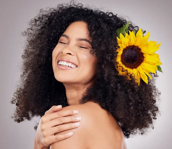 Portrait, happy or face of black woman with sunflower in hair in studio for spring time, luxury spa or self care. Aesthetic, beauty facial or girl model with plant for skincare, cosmetic or makeup.