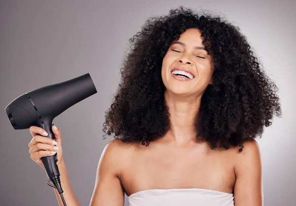 Face, beauty and black woman with hair dryer in studio isolated on gray background. Haircare, aesthetic or happy female model with machine to dry hairstyle after salon treatment for growth or texture.