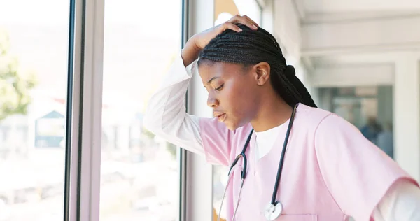 Nurse, stress thinking and hospital window for relax breathing, stress relief and healthcare worker frustrated or overworked. Black woman, employee burnout and anxiety headache working in clinic.