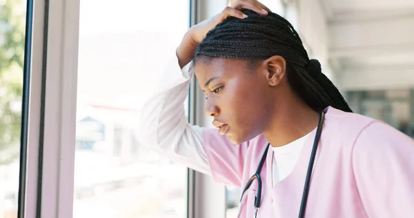 Nurse, stress thinking and hospital window for relax breathing, stress relief and healthcare worker frustrated or overworked. Black woman, employee burnout and anxiety headache working in clinic.