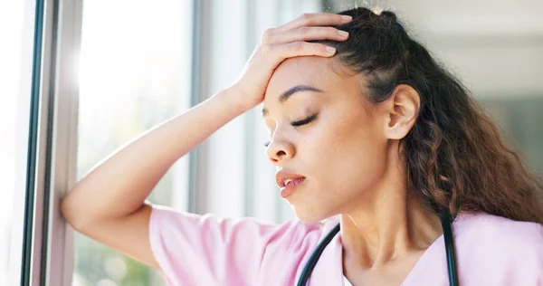 Nurse, thinking or stress headache by window in hospital, clinic or wellness theater and mental health burnout or anxiety. Exhausted, fatigue or tired healthcare woman in surgery mistake or work risk.