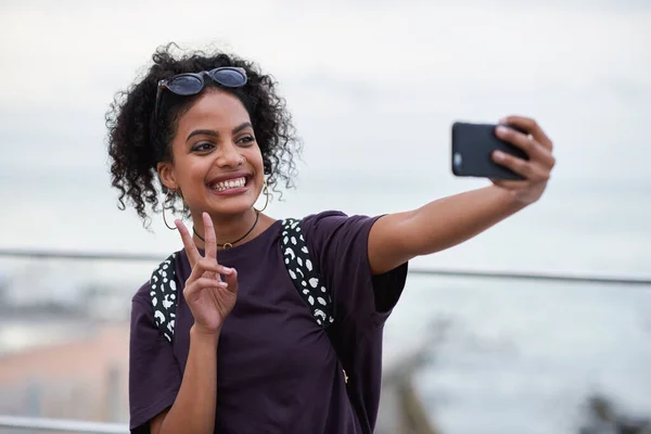 Selfie, peace sign and smile of black woman in city taking pictures for happy memory. Travel, street and female with v hand gesture, having fun and enjoying time while taking photo for social media