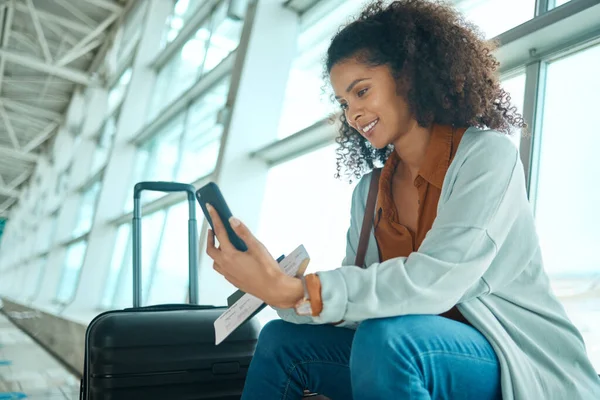 Travel ticket, phone and black woman at airport on a video call waiting for plane and flight. Online, mobile connection and smile of a happy young female sitting at airplane terminal for transport.