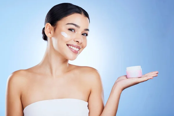 Woman, face and smile for skincare moisturizer, cosmetics or beauty against a blue studio background. Portrait of happy female smiling with product, lotion or cream for facial treatment on mockup.