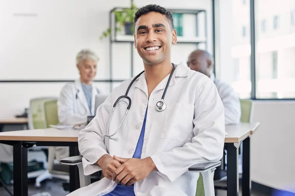 Young doctor, man and portrait at hospital desk with smile for healthcare, planning and teamwork. Professional leader, doctors and expert in health, wellness and happy in clinic with group at table.