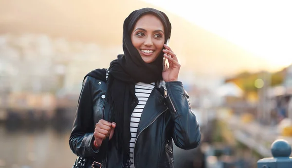 Phone call, muslim and woman talking in city, chatting or speaking to contact outdoors. Dubai, thinking and happy female with 5g mobile for networking, conversation or discussion in town at sunset
