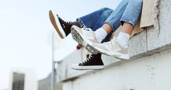 Shoes, legs and couple on rooftop in the city sitting together, have fun and bonding. Fashion sneakers, style and friends kick feet on building edge, enjoy weekend, freedom and holiday in urban town.