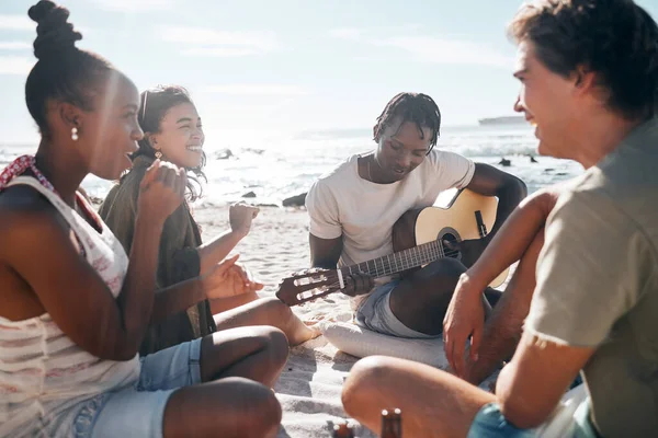 Couple of friends, playing and guitar by beach, ocean or sea in holiday vacation, summer travel or social gathering. Smile, happy and bonding diversity people with musical instrument in relax picnic.