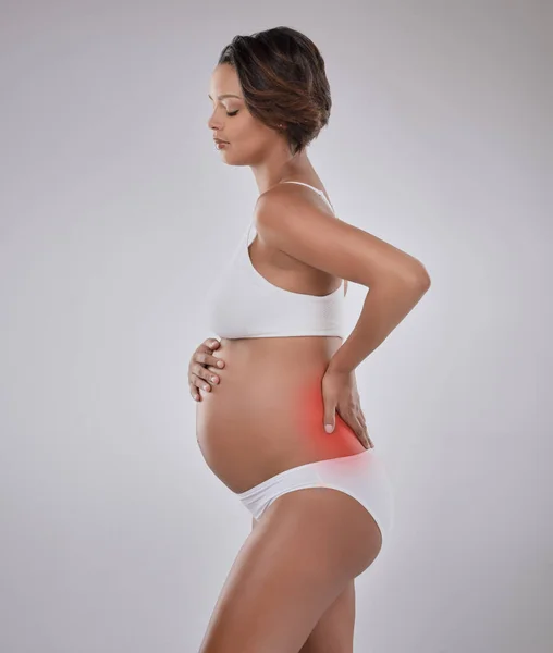 The painful side of pregnancy. Studio shot of a beautiful young pregnant woman experiencing back pain against a gray background