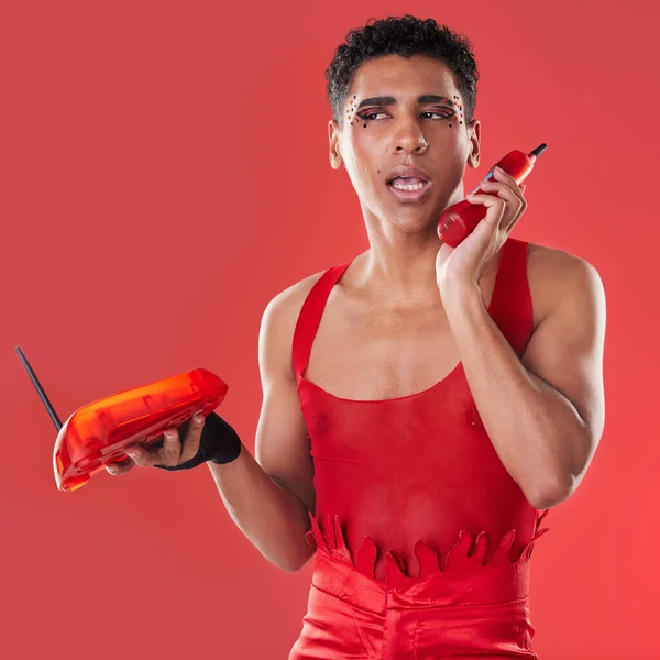 Phone call, beauty and gay man talking with a sassy attitude and red outfit in a studio. Conversation, mobile and beautiful lgbtq male with a cosmetics, makeup and style isolated by a red background
