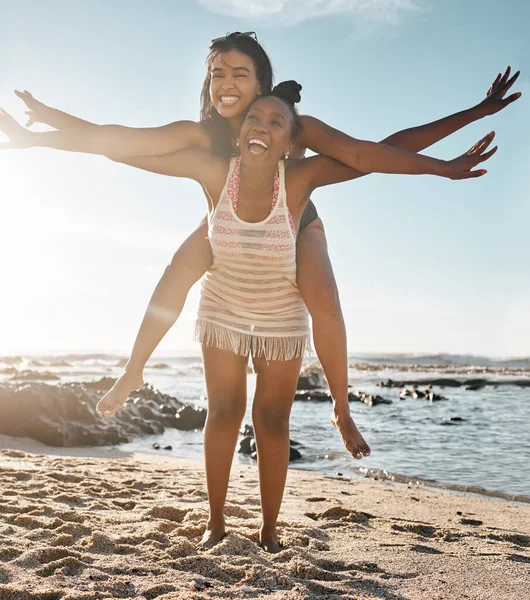 Friends, laughing or piggyback airplane by beach, ocean or sea in social gathering, vacation comedy or summer holiday. Smile, happy or black woman carrying girl in travel fun, bonding or comic games.