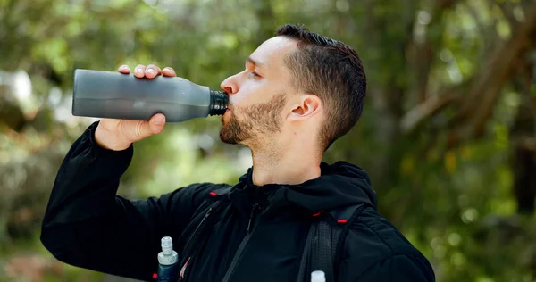 Hiking, nature and man drinking water in bottle while on outdoor adventure trail hike in forest. Travel, freedom and healthy young guy enjoying refreshing drink for hydration while trekking in woods
