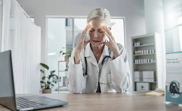 Headache, stress and female doctor in her office with a laptop in the hospital after a consultation. Frustrated, burnout and senior woman healthcare worker working with a migraine in a medical clinic.