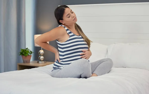 Pregnant, bed and woman with back pain, maternity issues and anxiety with ache, muscle strain and cramps. Pregnancy, female or lady in bedroom, contractions and anxious with health problems or stress.