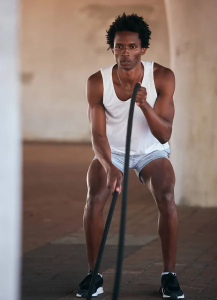 Exercise, fitness and black man with battle ropes for training workout in the city outdoors. Sports, energy and male body builder or athlete with heavy rope for strength, power or health in street