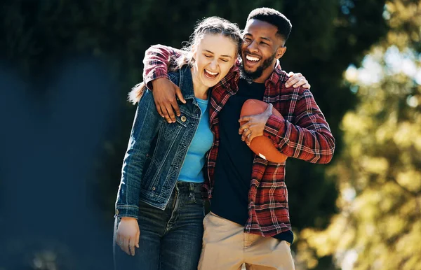 Love, diversity couple and laughing in nature, having fun and playing football outdoors. Comic, interracial romance and happy black man and woman hug, laugh at funny joke and enjoying time together