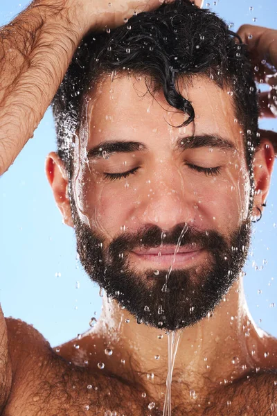 Washing, hair and man in studio for skincare, grooming and hygiene against blue background. Haircare, body care and guy model relax in shower, happy and isolated on water splash, cosmetic or wellness.