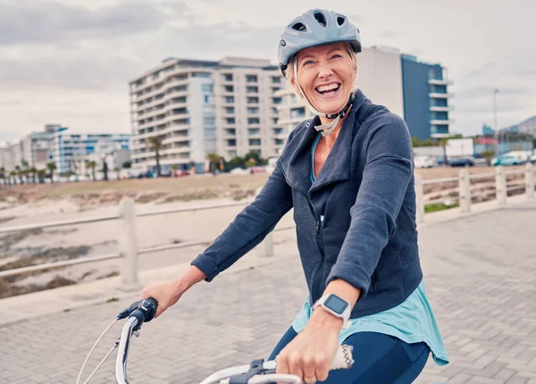 Fitness, promenade and woman riding a bicycle for exercise, health and wellness by the beach. Sports, smile and portrait of happy senior female cyclist cycling for outdoor cardio workout or training