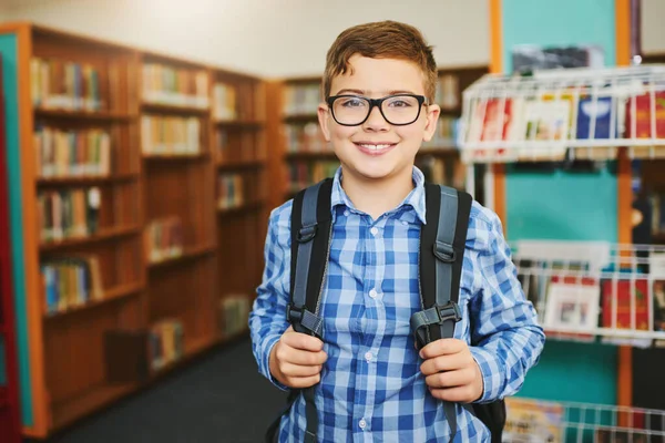 Im always down for an adventure. Portrait of a cheerful young boy wearing a schoolbag while standing inside of library during the day
