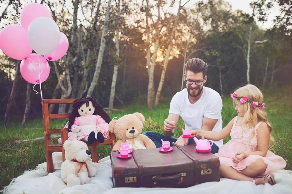 Keep your pinky up when you drink tea daddy. a cheerful daughter and father having a tea party with a bunch of stuffed toys in the middle of a garden