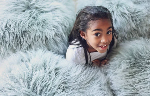 Relax, happy and portrait of a child with pillows in her modern bedroom in her home. Happiness, smile and girl kid resting, having fun and being playful with fluffy blankets in her room at a house