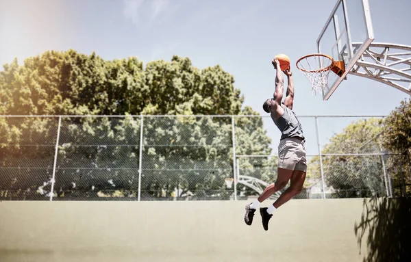 Full length of basketball player dunking a ball into the net during a match on a court. Fit and active athlete jumping to score during a competitive game. Healthy athletic african man in action.
