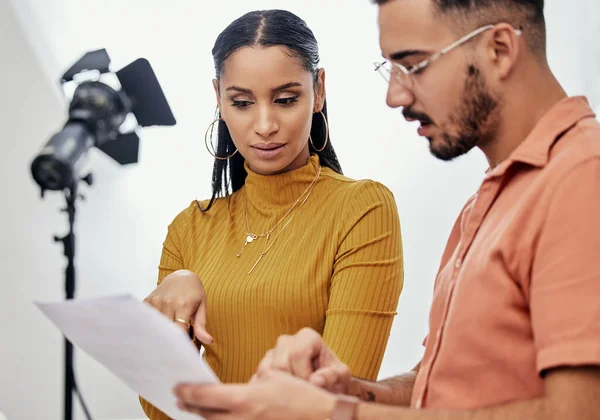 Documents, collaboration or planning with a photographer and model talking in a studio for creative production. Teamwork, designer or fashion with a designer man and woman at work on a magazine shoot.