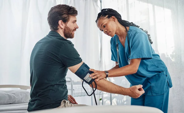 Nurse, doctor and man with blood pressure test in hospital for heart health or wellness. Healthcare, hypertension consultation and medical physician with patient for examination with sphygmomanometer.