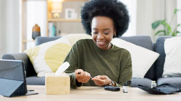 Happy African American woman using a glucose monitoring device at home. Smiling black female checking her sugar level with a rapid test result kit, daily routine of diabetic care in a living room.