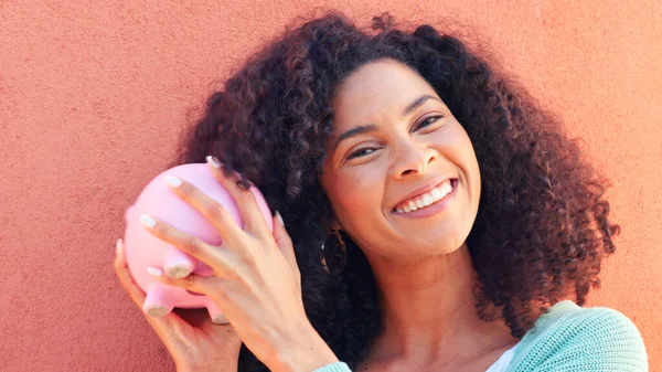 Piggy bank, cash and savings with a black woman listening to money in a pig outside on a pink wall background. Happy, smile and success with a young female confident with her finance and budget.