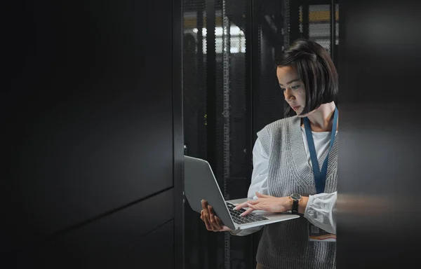 Woman with laptop, datacenter and information technology, engineer and server room with software update. Tech industry, cybersecurity and network with Asian female setting up firewall and database.