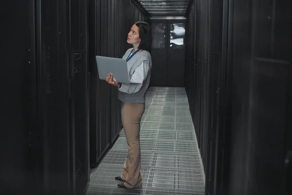 Woman with laptop, server room and information technology, technician and datacenter with software update. Tech industry, cybersecurity and network with Asian female setting up firewall and database.