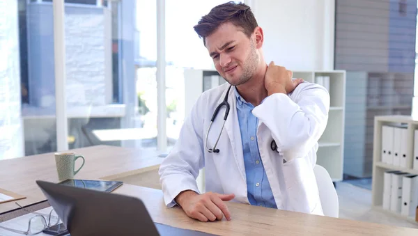Man, doctor and laptop with neck pain, ache or tension sitting by office desk in stress or discomfort at hospital. Healthcare male suffering holding painful area from work injury, bruise or sore.