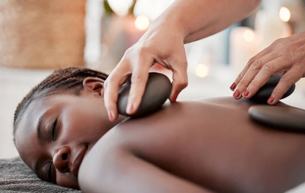 Black woman, hot stone massage, spa and hands of masseuse, holistic and wellness, therapy and treatment. Health, peace of mind and rocks with zen, stress relief for people and back skin detox.