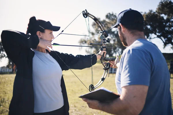 Archery, bow and arrow with woman and coach, aim at target with sports outdoor, combat training and weapon. Coaching, learning and teaching with female and man at shooting range, archer and help.