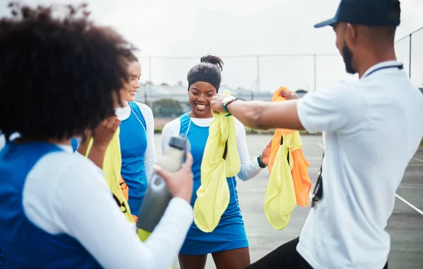 Coach, vest or team in netball training game, workout or exercise for a match on sports court. Teamwork, fitness group or manager giving bibs to excited athlete girls with happy smile in practice.