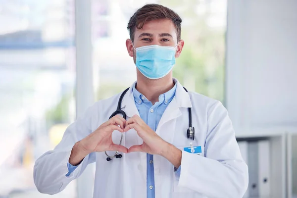 Covid, portrait and doctor with hand heart sign at hospital for healthcare, innovation and symbol of trust. Emoji, hands and face of cardiovascular surgeon with mask for corona compliance at a clinic.