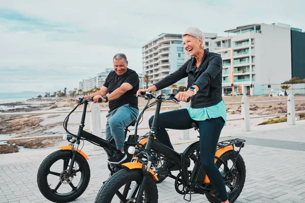 Senior couple, electric bike and smile by the beach for fun bonding cycling or travel together in the city. Happy elderly man and woman enjoying cruise on electrical bicycle for trip in Cape Town.