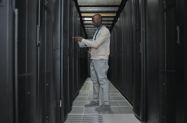 Laptop, maintenance and server room with IT black man for research, engineer working in dark data center. Computer, cybersecurity and analytics with male programmer problem solving or troubleshooting.