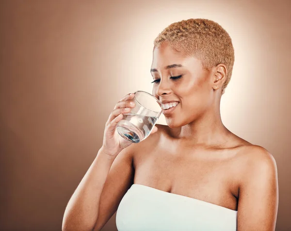 Drinking water, black woman and glass for health on a brown background for skincare or diet. Aesthetic model person smile for clean and sustainable liquid for healthy lifestyle and wellness in studio.