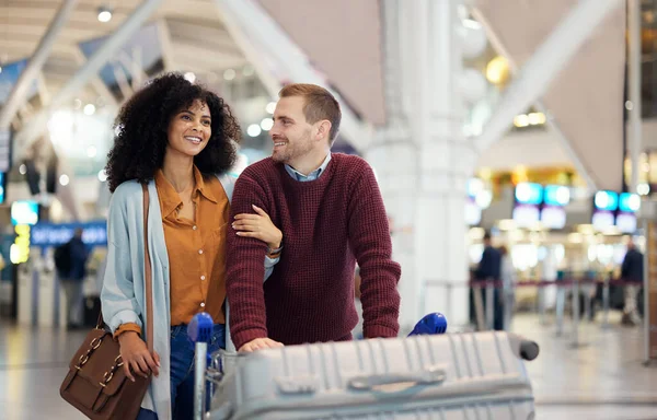 Travel, happy and love with interracial couple in airport for vacation, journey and transportation. Relax, smile and luggage with man and black woman on holiday trip for tourism, flight or departure.