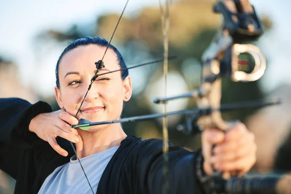 Archery bow, woman aim and shooting range for competition, game or practice at an outdoor sports or park. Hunter or person face with arrow for gaming, adventure and hunting with focus on target.