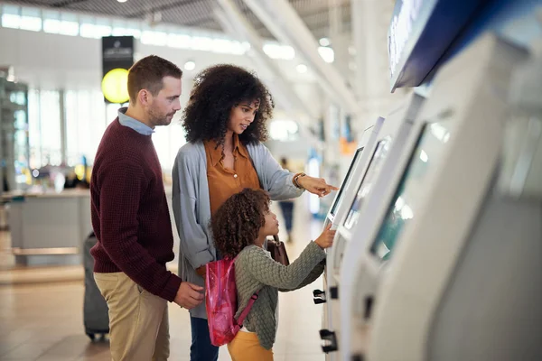 Family, self service and travel at airport for check in, registration or booking flight online together. Mother, father and child at kiosk for ticket and planning traveling vacation, trip or journey.