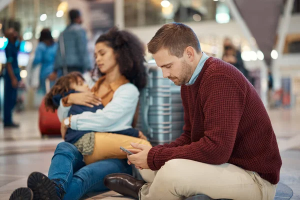 Phone, tired and interracial family waiting at the airport for a delayed flight. Contact, late and man on a mobile app with a black woman and child sleeping during problems with travel on a trip.
