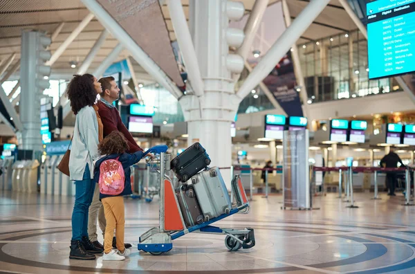 Airport, flight schedule and family with suitcase trolley for holiday, vacation or immigration travel and time check. Luggage of diversity parents or mother and father with child or kid in lobby.