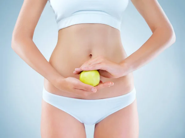 Healthy diets build healthy bodies. an unidentifiable young woman posing with an apple in front of her stomach in studio