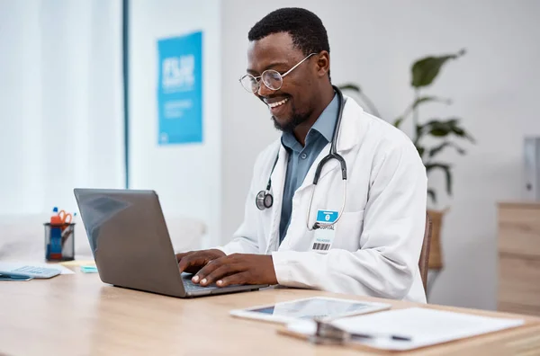 Black man, doctor and laptop with smile in healthcare for research, medicine or PHD at clinic desk. Happy African American male medical professional smiling, working or typing on computer at hospital.