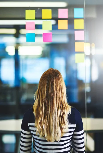 Driving creativity with critical thinking. Rearview shot of a woman having a brainstorming session with sticky notes at work