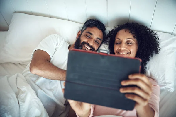 Forget the cinema, lets stay in bed. a mature couple using a digital tablet while relaxing together in bed