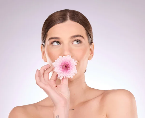 Woman, flowers and daisy for skincare, cosmetics and natural aesthetic wellness on studio background. Young model, beauty and pink plants for sustainability, floral perfume or clean vegan dermatology.